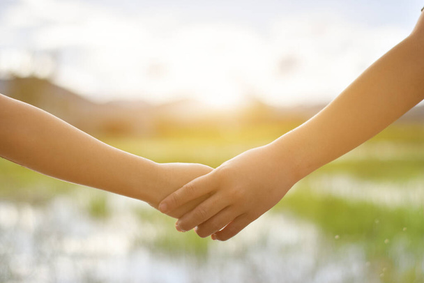 Sahada birbirini tutan iki çocuğun elleri. Karşılıklı yardım ve dostluk kavramı - Fotoğraf, Görsel