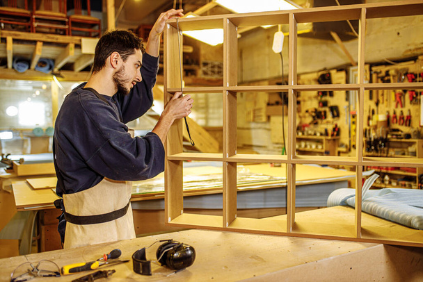 hardworking carpenter measures handmade shelves - Foto, Bild