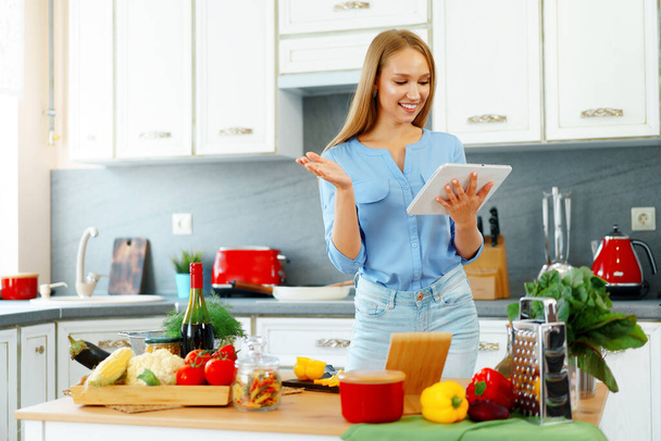 Young beautiful caucasian woman cooking and using her digital tablet in kitchen - Foto, imagen