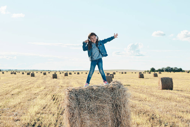 A cute little girl listens to music and dances on a haystack. - Photo, Image