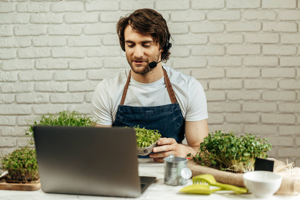 Handsome bearded man sells plant sprouts and seedlings online using laptop - Foto, imagen