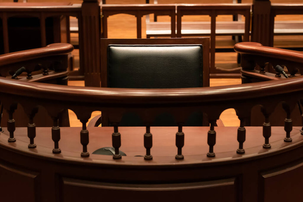 Un testigo de pie con un asiento negro en la sala de la corte frente al tribunal cuando los testigos testifican de pruebas para juzgar, se sentarán aquí para el testimonio de los testigos, es estilo vintage o retro - Foto, Imagen