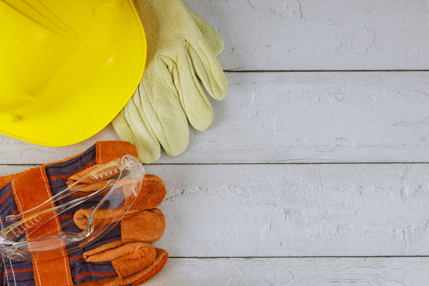 Equipo de protección de trabajo de construcción con casco amarillo y un par de guantes de trabajo gafas de seguridad sobre un fondo blanco de madera - Foto, Imagen