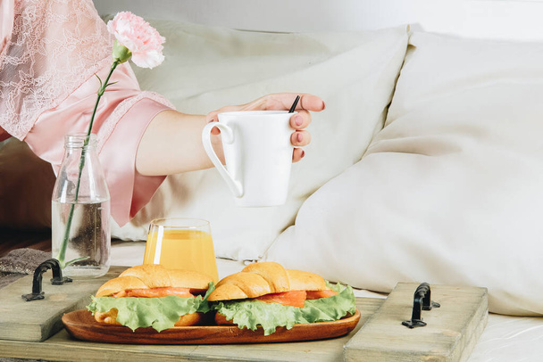  Két croissant hallal és zöld salátával, narancslével, kávéval és egy virággal. Reggeli az ágyban - Fotó, kép