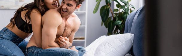 horizontal crop of woman in jeans and bra sitting on bed with muscular boyfriend  - Photo, Image