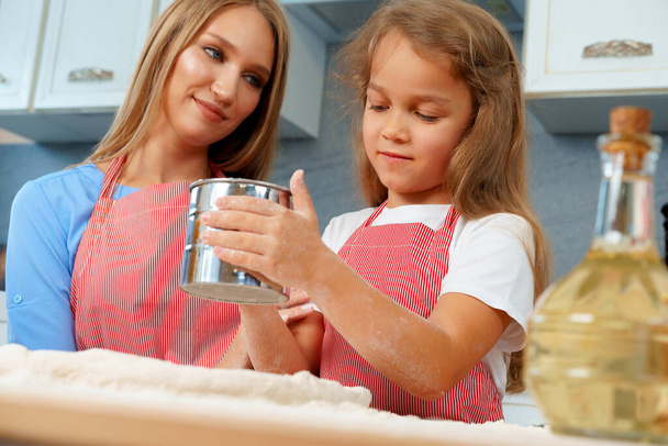 Mother and her little daughter preparing dough in kitchen - Foto, Imagen