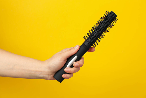 Female hand holds hair brush on yellow background, space for text - Photo, Image