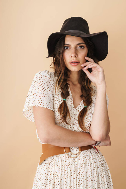 Photo of brunette beautiful woman in hat posing and looking at camera isolated over beige background - Foto, imagen