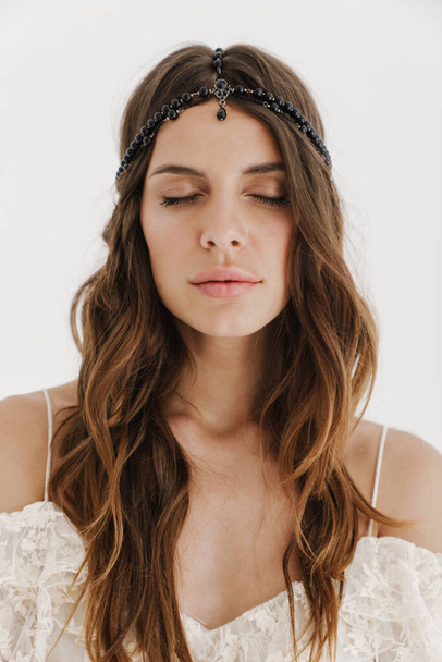 Φωτογραφία της χαλαρής γυναίκας φορώντας κοσμήματα μαλλιά θέτουν με τα μάτια κλειστά στην κάμερα απομονώνονται σε λευκό φόντο - Φωτογραφία, εικόνα