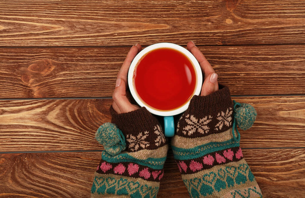 Feche duas mãos de mulher segurar e abraçar grande xícara cheia de chá preto ou chá de frutas vermelhas sobre mesa de madeira marrom, vista superior elevada, diretamente acima
 - Foto, Imagem