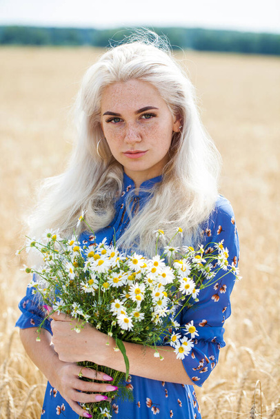 close up portrait of a young blonde girl with a bouquet of chamomile in a field - Фото, изображение