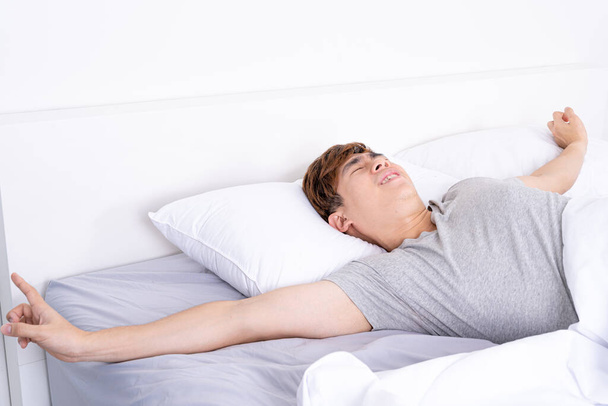 Joven hombre asiático estirándose en la cama después de despertar de la buena cama cómoda. Concepto de atención médica o de vida diaria. - Foto, Imagen