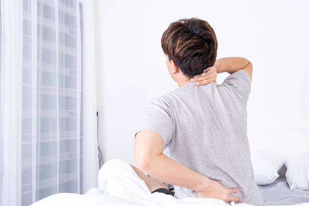 Nuori mies kärsii niskasta ja selkäkivuista epämukavasta sängystä. Terveydenhuollon lääketieteellisen tai jokapäiväisen elämän käsite. - Valokuva, kuva