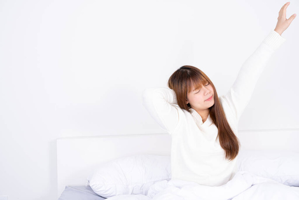 Jonge Aziatische vrouw stretching in bed na wakker worden uit het goede comfortabele bed. Gezondheidszorg medisch of dagelijks leven concept. - Foto, afbeelding