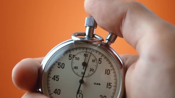 Reloj de mano masculino con cronómetro analógico sobre fondo de color naranja. El tiempo comienza con el viejo cronómetro hombre presiona el botón de inicio en el concepto de deporte. Concepto de gestión del tiempo. - Metraje, vídeo