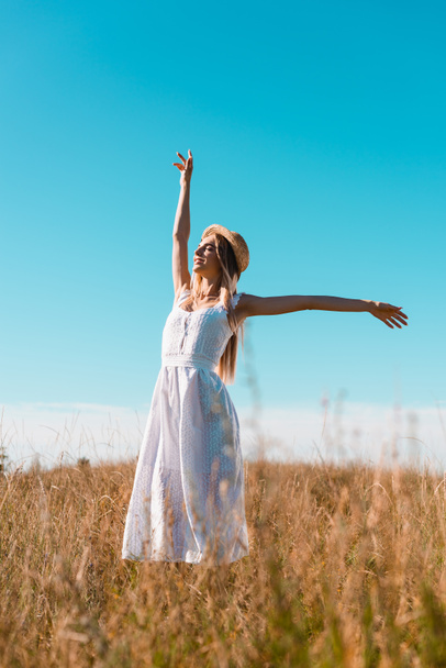 selective focus of sensual woman in white dress standing with outstretched hands and closed eyes on grassy field - Photo, Image