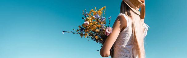fiatal nő nyári ruhában gazdaság csokor vadvirágok ellen kék ég, vízszintes kép - Fotó, kép