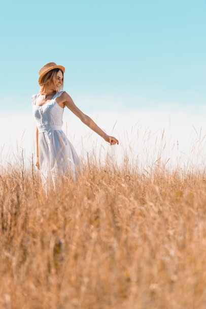 白いドレスとわらの帽子のブロンドの女性の選択的な焦点は、草の牧草地で私に従うジェスチャーを示す - 写真・画像