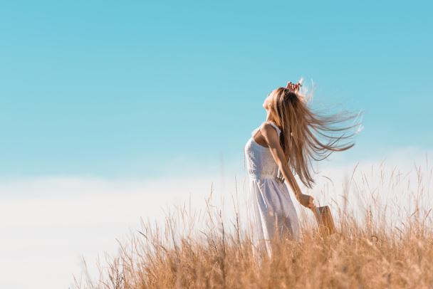 草の丘の上に手を上げながら、白いドレスを保持わら帽子でブロンドの女性の選択的な焦点 - 写真・画像