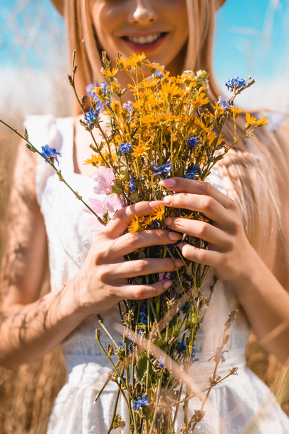 partial view of young woman holding bouquet of wildflowers, selective focus - Foto, Bild