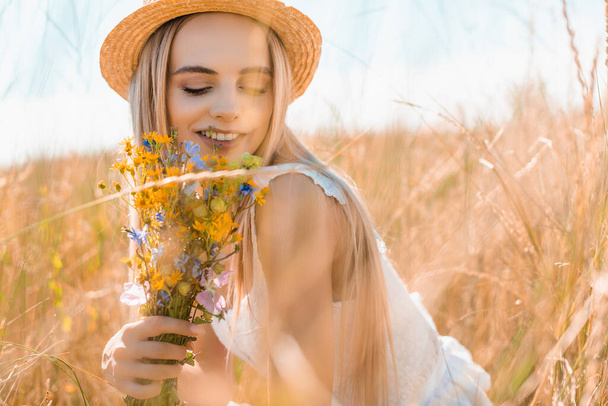 selective focus of sensual woman in straw hat holding wildflowers in grassy field - Foto, Imagem