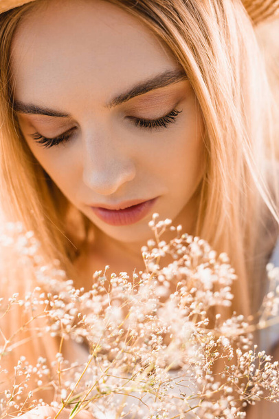 portret zamyślonej blondynki w pobliżu dzikich kwiatów, selektywne skupienie - Zdjęcie, obraz