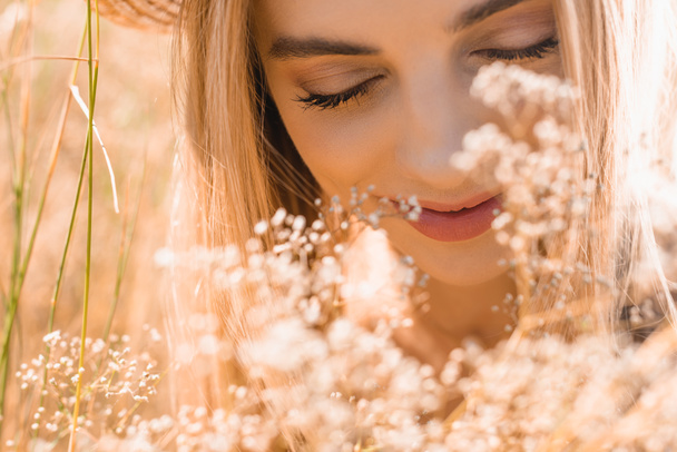 retrato de mulher loira com olhos fechados perto de flores silvestres, foco seletivo - Foto, Imagem