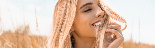 horizontal image of excited blonde woman touching hair while looking away  - Photo, Image