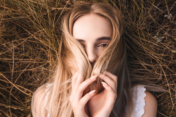 ylhäältä näkymä nuori blondi nainen peittää kasvot hiukset makaamassa ruohoa ja katsot kameraa - Valokuva, kuva