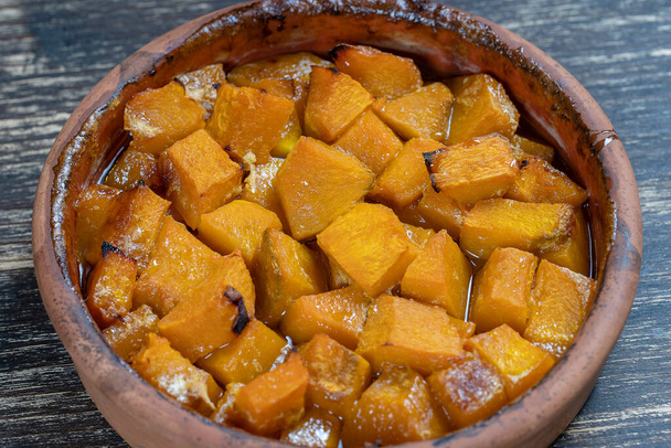 Baked yellow pumpkin with honey, olive oil and spices on a plate on the wooden table. Vegetarian food. Close up - 写真・画像
