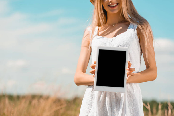 vista parziale di giovane donna in abito bianco che mostra tablet digitale con schermo bianco  - Foto, immagini