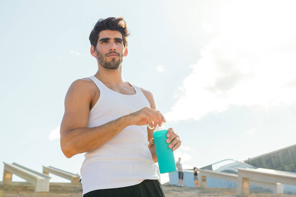 schöner Sportler mit einer Flasche Wasser in einer Trainingspause, Konzept des urbanen Sports und gesunden Lebensstils, Kopierplatz für Text - Foto, Bild