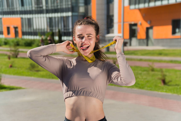 funny naughty girl holds a centimeter tape in her hands. The concept of improper weight loss woman fitness trainer in the park - Foto, immagini