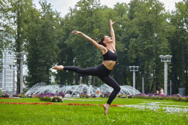 slightly not sharp photo. Attractive girl in sportswear makes beautiful jumps on the grass in the city park. - Фото, зображення