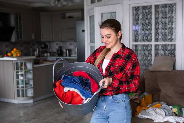 Happy woman in a plaid shirt holds a full laundry basket - Foto, imagen