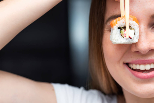 Portrait of woman holding sushi roll on eye - Zdjęcie, obraz
