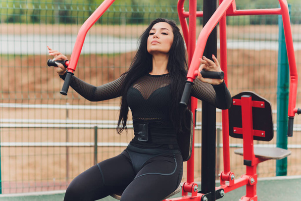 Woman smiling while exercising upper body using weights machine outside. - Foto, imagen