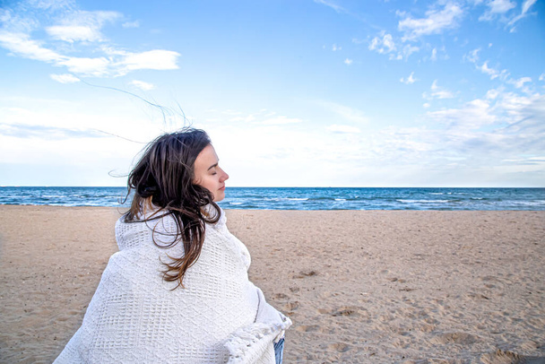 Egy fiatal nő a tenger mellett, egy kényelmes takaróval borítva. . - Fotó, kép