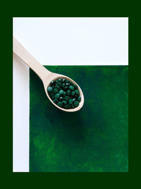 Green hawaiian spirulina in tablespoons pills in wooden spoon on green background. Super food, healthy lifestyle, healthy supplements, superfoods in cooking concept - Photo, Image