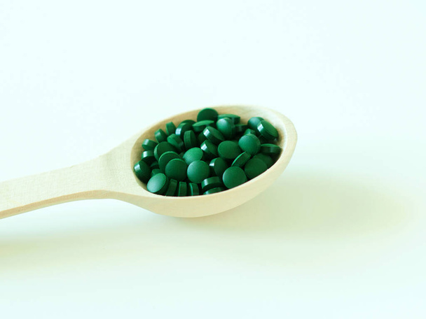Green hawaiian spirulina in tablespoons pills in wooden spoon. Super food, healthy lifestyle, healthy supplements, superfoods in cooking concept - Fotó, kép