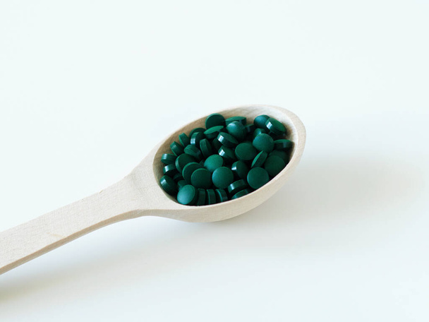 Green hawaiian spirulina in tablespoons pills in wooden spoon. Super food, healthy lifestyle, healthy supplements, superfoods in cooking concept - Фото, зображення
