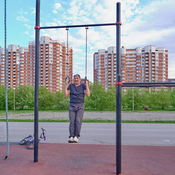 VA sênior asiático homem formação no esporte chão no parque da cidade no fundo de uma paisagem urbana. Pendurado nos anéis. Estilo de vida Desfoque de movimento
 - Foto, Imagem