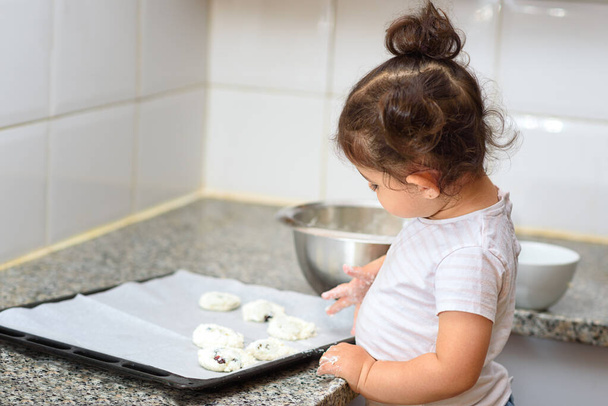 Little kid girl making cookies on marble table. Happy family funny child are preparing the dough, bake cookies in the white kitchen. - Photo, Image