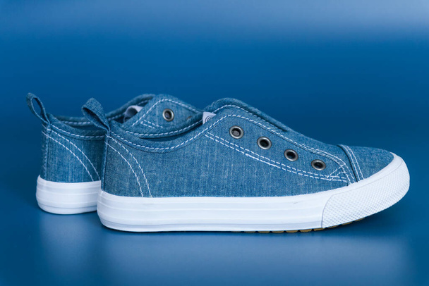 Blauwe kindersneakers met witte zolen zonder veters op een blauwe achtergrond - Foto, afbeelding