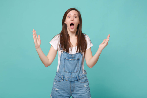 Shocked young brunette woman girl in casual denim clothes isolated on blue turquoise background. People lifestyle concept. Mock up copy space. Gesturing demonstrating size with horizontal workspace - Foto, Imagen
