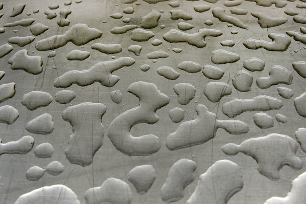 Oppervlakte met druppels. Waterdruppels van verschillende vormen op een vlak grijs gekrast oppervlak. Achtergrondtest na regenclose-up. - Foto, afbeelding