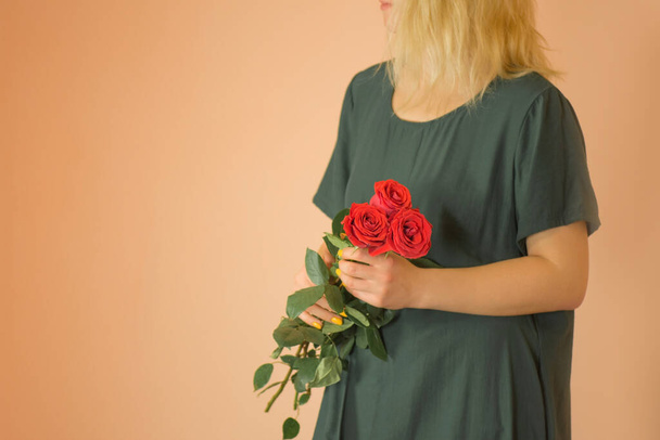 Egy vörös rózsás csokor. Tavaszi csokor vörös rózsa a nők kezében világos bézs háttér - Fotó, kép