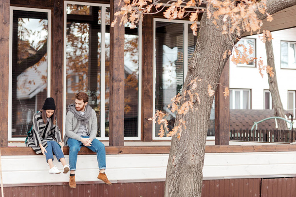 Happy young couple sitting outdoor, in front of their new home in autumn day - Fotografie, Obrázek