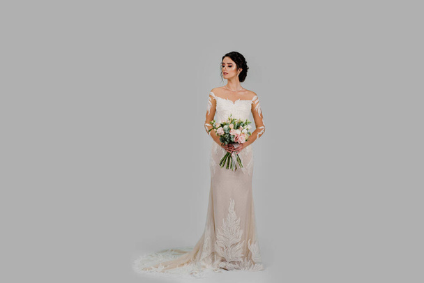 Невеста в белом свадебном платье с букетом выглядит слева в студии на белом пустом фоне. Реклама в социальных сетях для свадебного агентства и свадебного салона - Фото, изображение