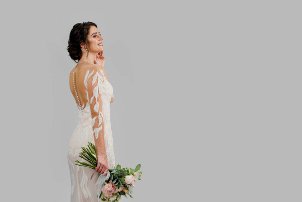 Menyasszony luxus esküvői ruha csokorral stúdióban fehér üres háttér jobb oldalon. Advert a szociális hálózatok esküvői ügynökség és menyasszonyi szalon - Fotó, kép